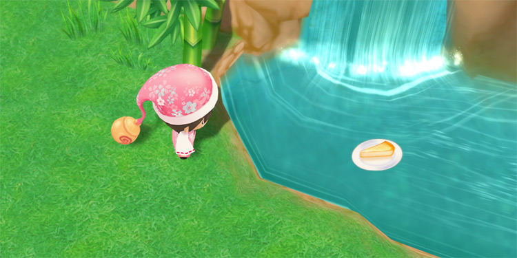 The farmer throws a Cheesecake into the Harvest Goddess’ waterfall. / Story of Seasons: Friends of Mineral Town